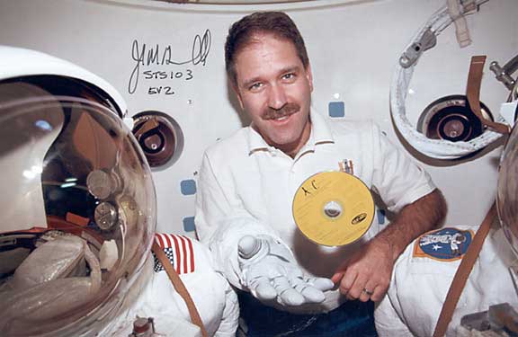 disk floating in space next to astronaut John Grunsfeld's hand
